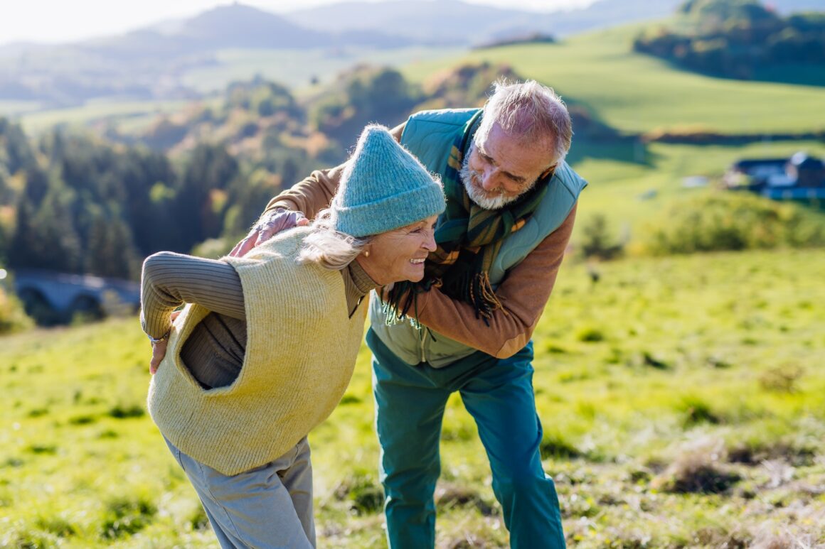 Senior woman with having pain in back during autumn walk, her husband taking care of her.