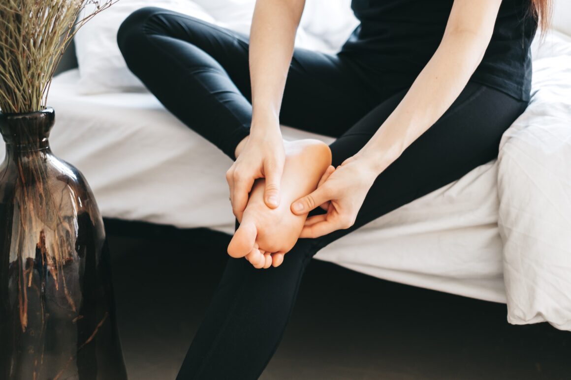 Young woman massaging her foot on the white bed after training or hard working day.