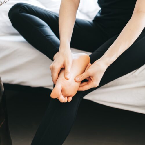 Young woman massaging her foot on the white bed after training or hard working day.